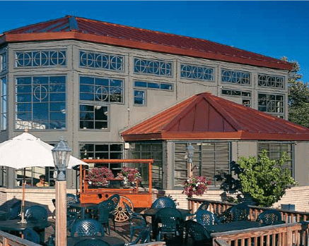 Restaurant exterior with outdoor seating, red roof, large windows, gray facade.