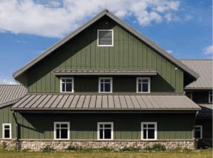 Green building with a stone base and a metal roof, against a cloudy sky.