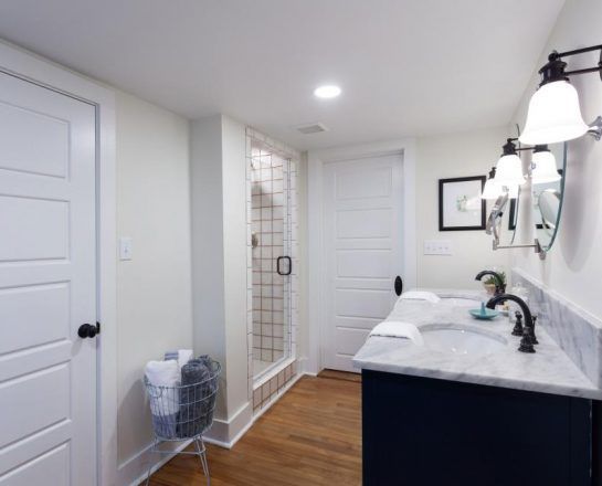Bathroom with navy vanity, marble countertop, glass shower, and white doors.