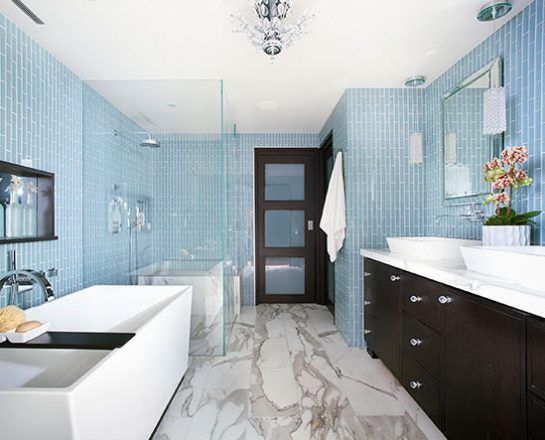 Modern bathroom with blue tile walls, marble floors, a white tub, and a dark wood vanity.