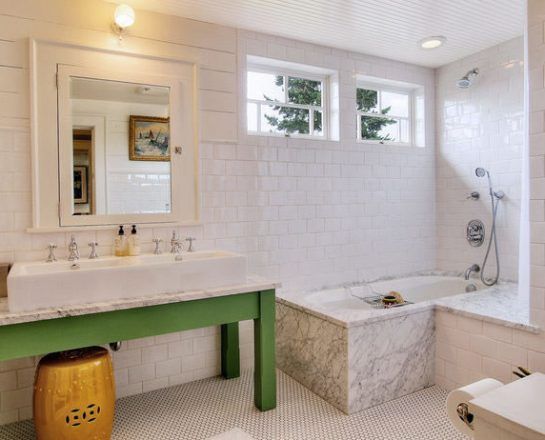 White tiled bathroom with a green vanity, marble tub, and small windows.