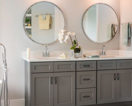 Gray bathroom vanity with two round mirrors, white countertop, and floral decor.