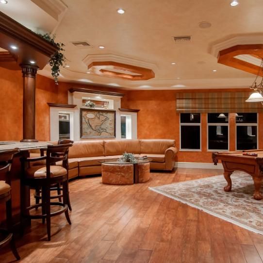 Spacious game room with pool table, bar, and seating. Orange walls, wood floors, and neutral furniture.