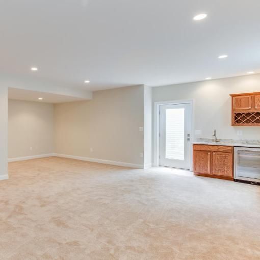 Empty basement room with tan carpet, beige walls, recessed lights, a wet bar, and a door.