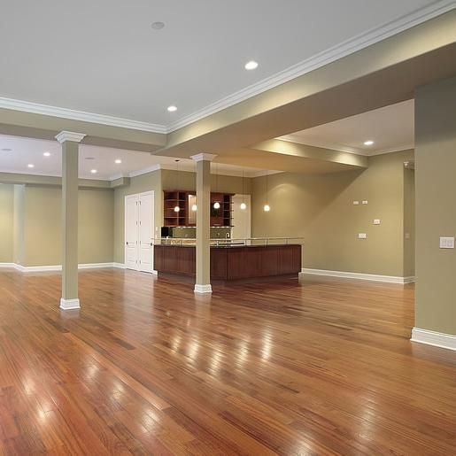 Spacious room with wooden floors, columns, and a kitchen island. Beige walls and recessed lighting.