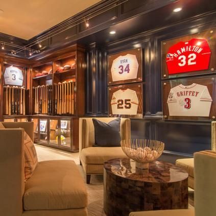 Baseball-themed room with jerseys, bats, memorabilia, seating. Dark blue walls, wood accents, and beige upholstery.