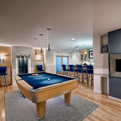 Pool table in a basement bar. Blue felt, hardwood floor, bar stools, and pendant lights.