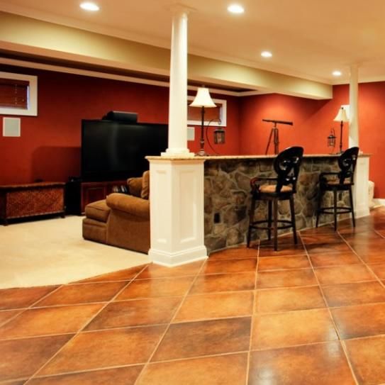 Finished basement with a bar, seating, TV, and red walls. Tile floor and white pillars.