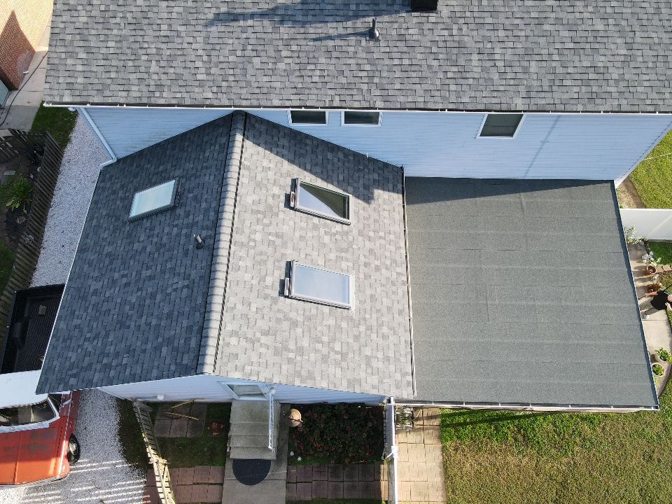 Overhead view of a house with gray shingle roof, a flat black roof, and a red car in the driveway.