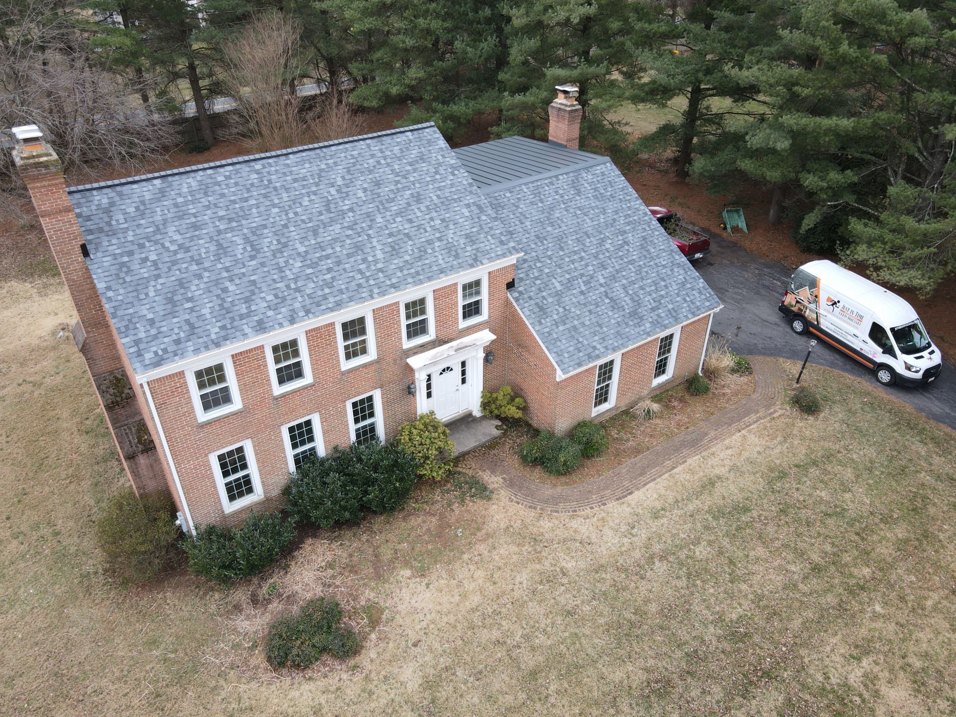 Two-story brick home with new gray roof; white van in driveway; trees in background.