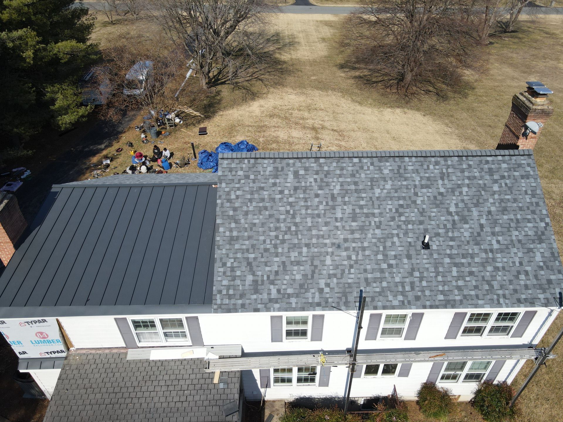 Aerial view of a two-story house with a gray shingle roof on one side and a dark gray metal roof on the other.