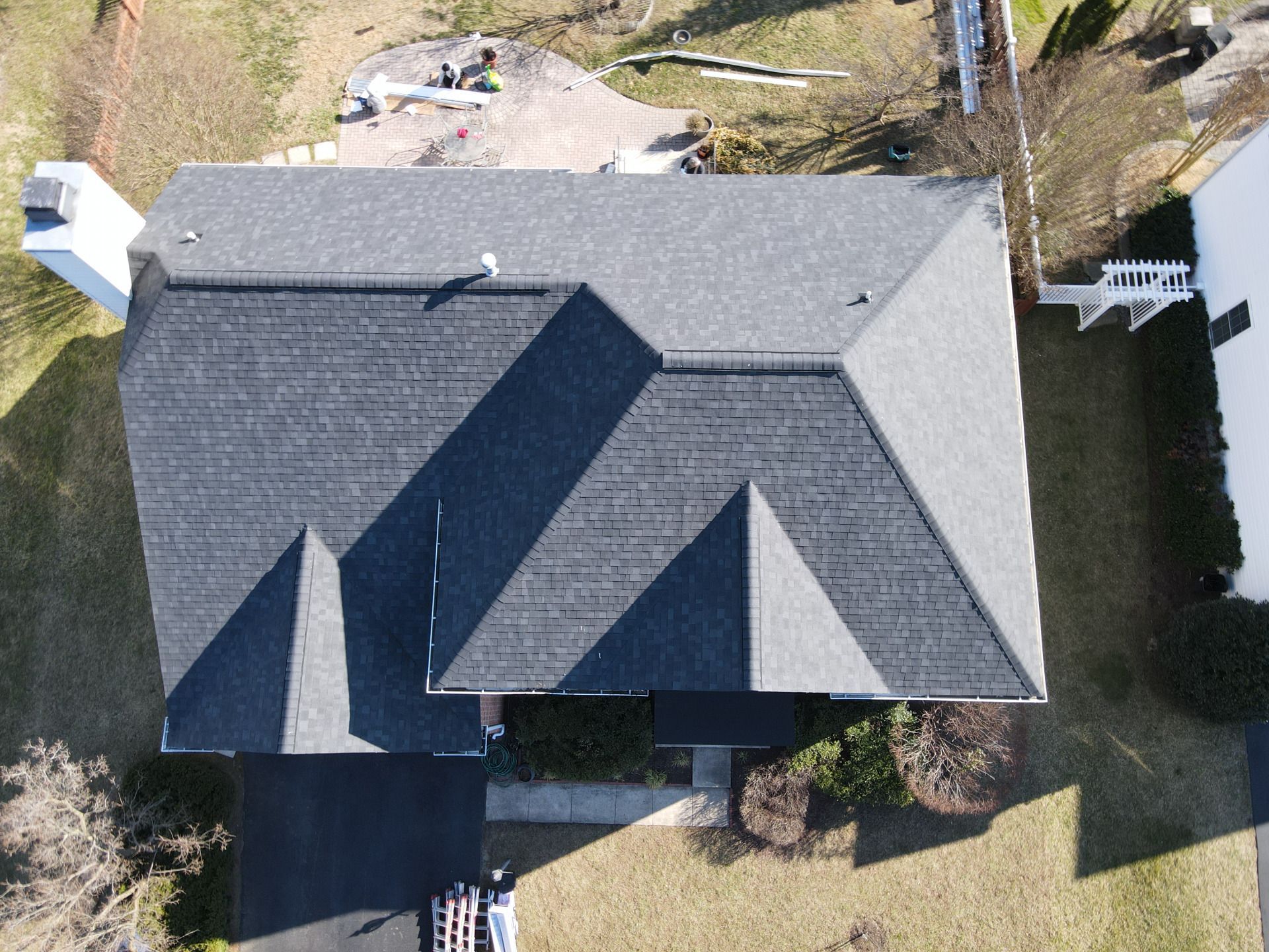 Overhead view of a dark-roofed house with a chimney and driveway on a sunny day.