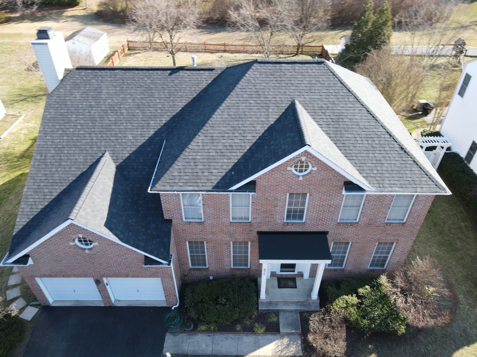 Brick house with dark gray shingle roof, garage, chimney, and front door; sunny day.