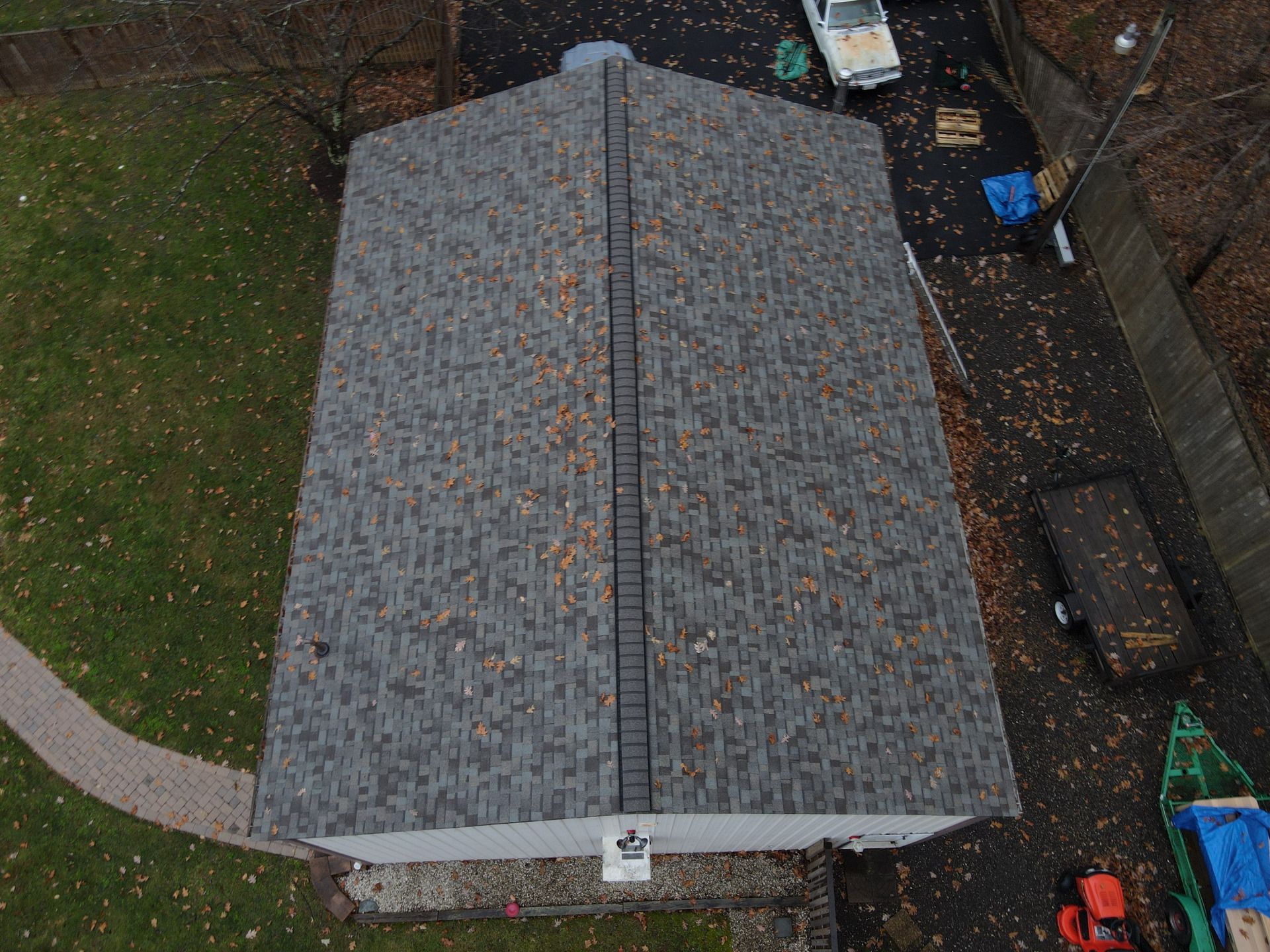 Overhead view of a house with a gray shingled roof covered in leaves, surrounded by a yard and driveway.