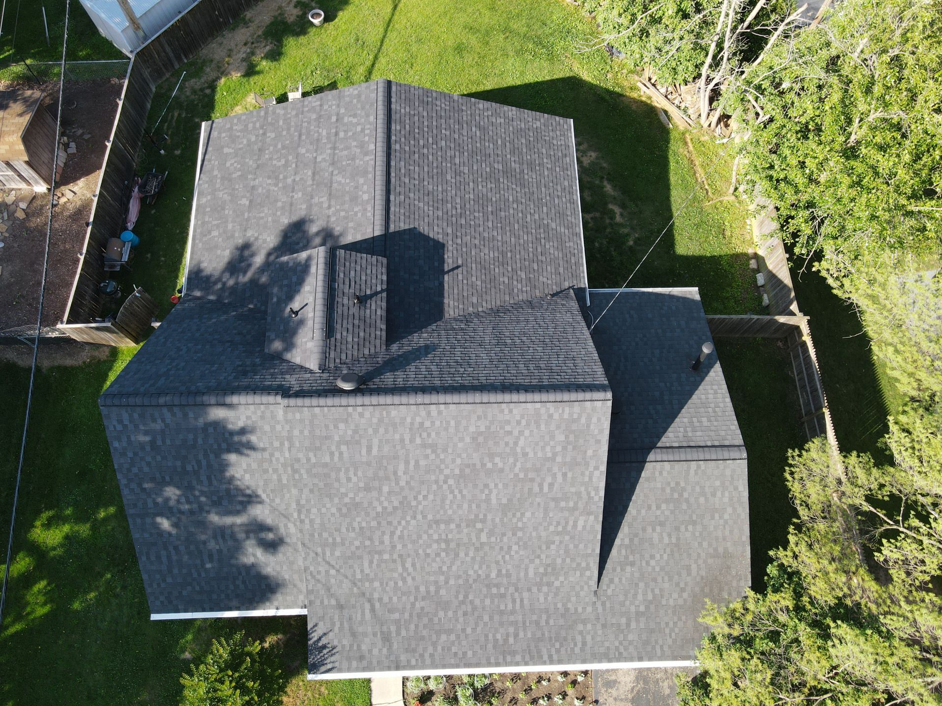 Overhead view of a house with a dark gray shingled roof, chimney, and green yard.