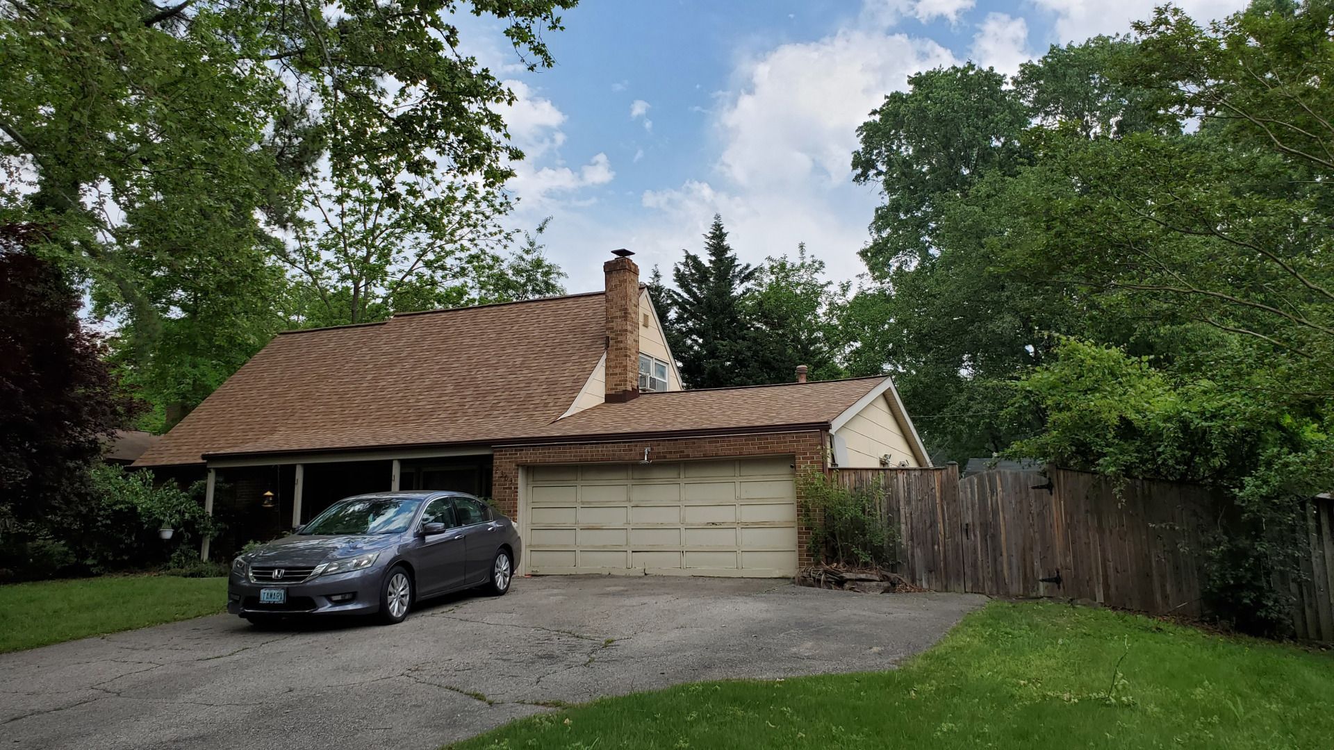 A gray car parked in front of a house with a brown roof and a garage.