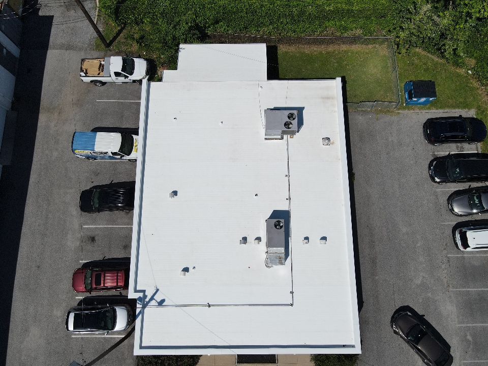 Overhead view of a white roof building with parked cars and a parking lot.