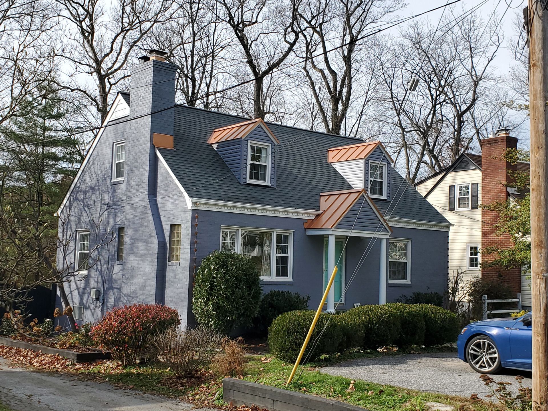 Blue house with copper roof accents, windows, and dormers; car parked in driveway.