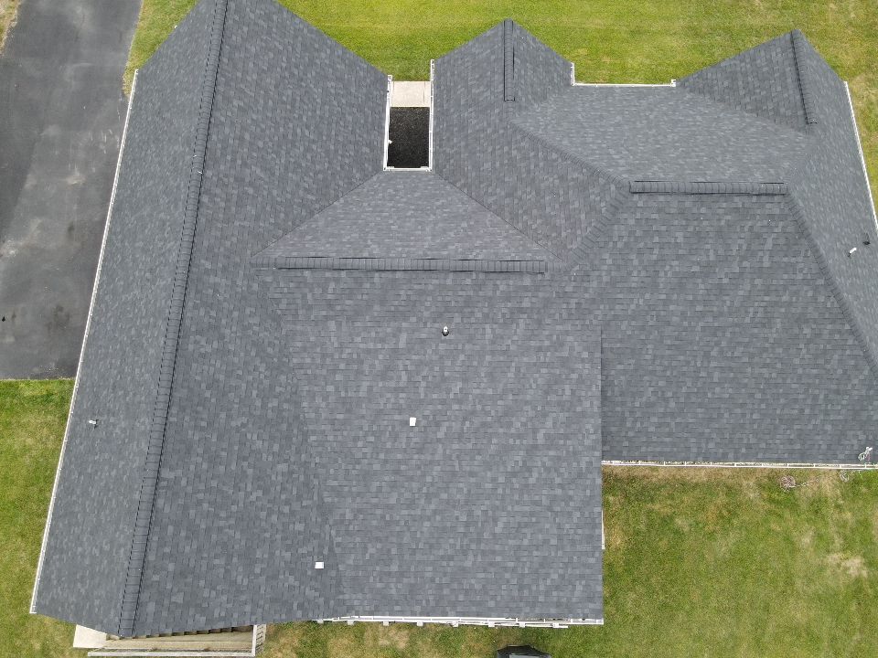 Aerial view of a dark gray shingled roof on a house with multiple gables and a skylight.