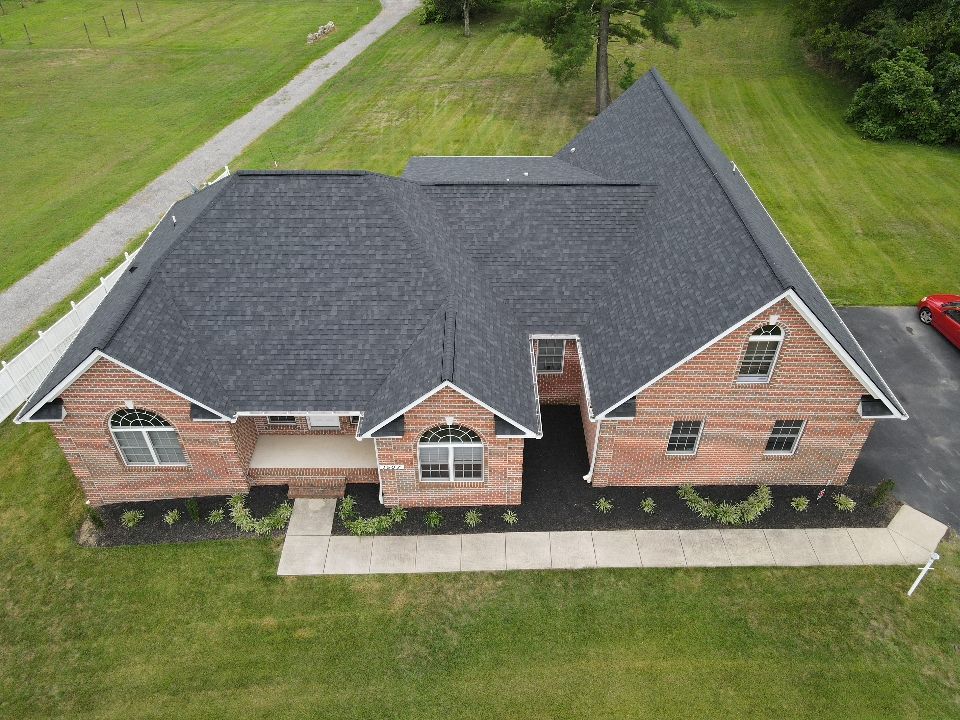 Aerial view of a brick house with a dark roof and surrounding green lawn.