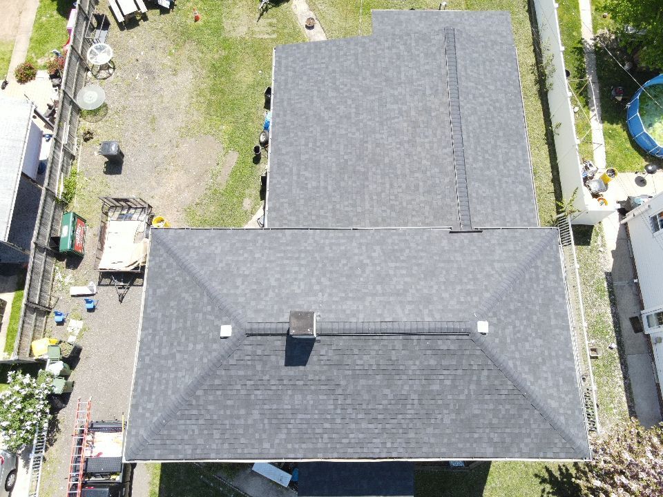 Overhead view of a house with a dark gray roof, surrounded by a yard, fence, and other buildings.