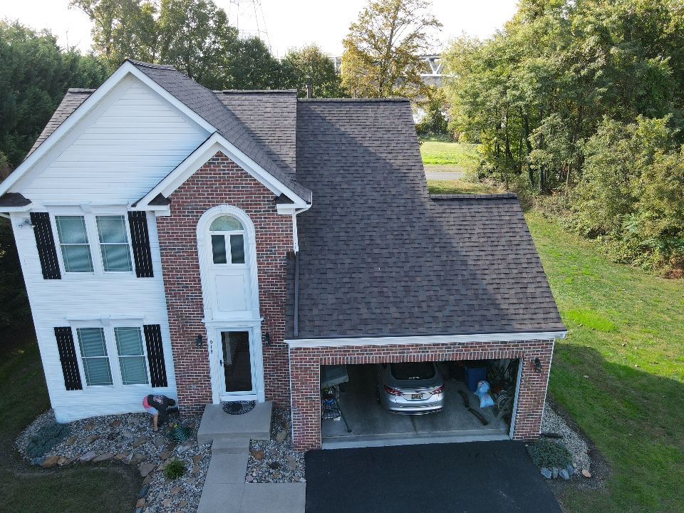 Two-story brick and white house with garage, car inside, trees, and a grassy lawn.