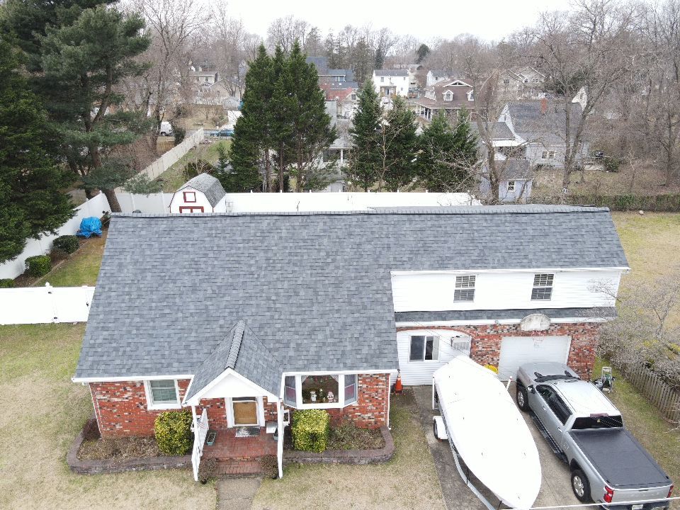 Overhead view of a two-story house with gray roof, red brick facade, and a boat on a trailer.