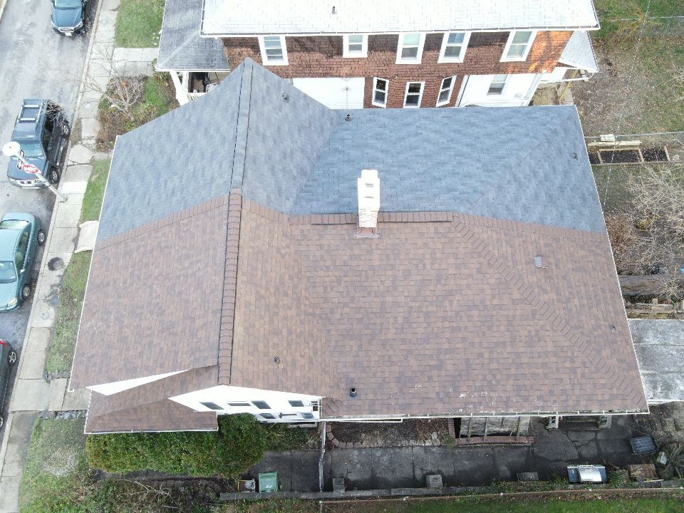 Overhead view of a house with brown and blue-gray shingles, a chimney, and parked cars on the street.