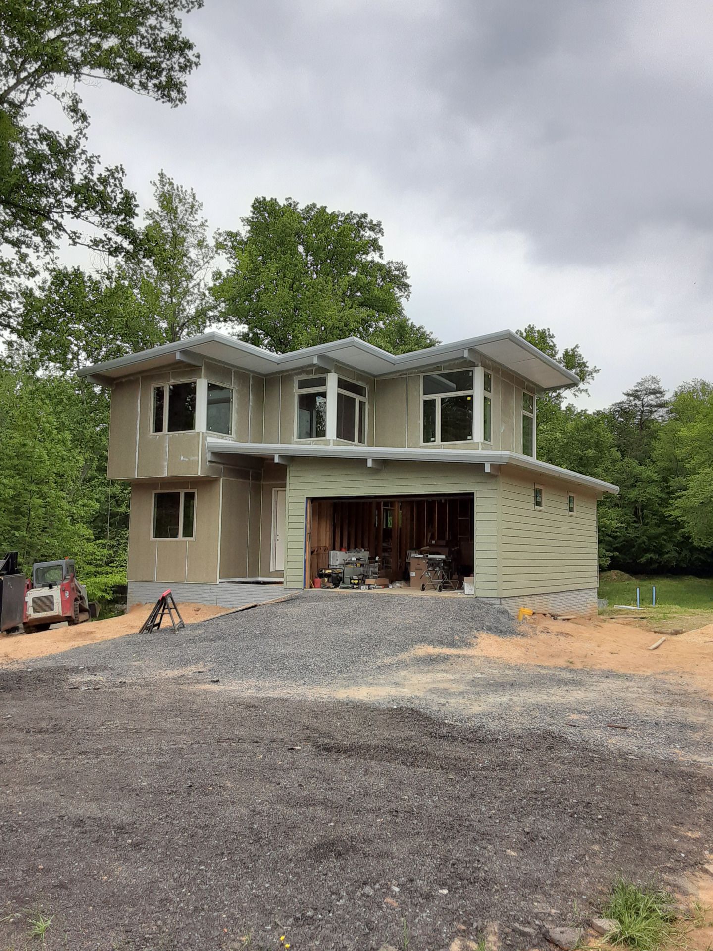 Two-story house under construction with unfinished exterior, garage, and gravel driveway.