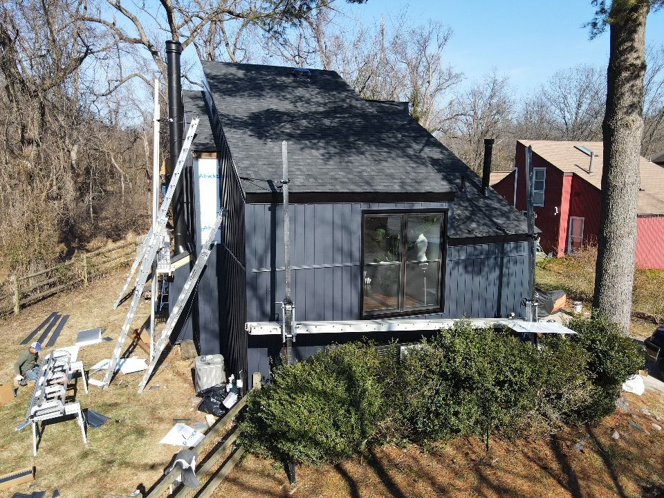 A dark gray, modern house with a sloped roof, surrounded by trees and a small fence.