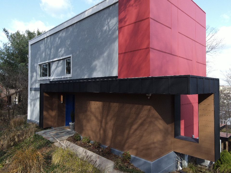 Modern house with gray, red, and brown exterior; blue door; low-angle view.