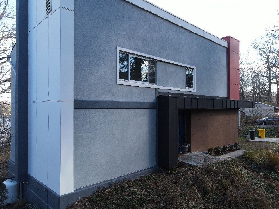Modern building with gray stucco, white accents, and a brown entry.