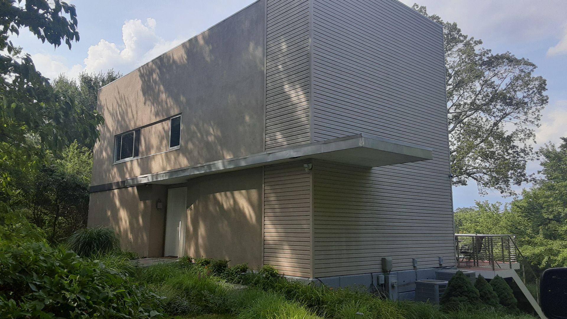 Modern two-story building with perforated facade, light gray walls, small windows, surrounded by green trees and grass.