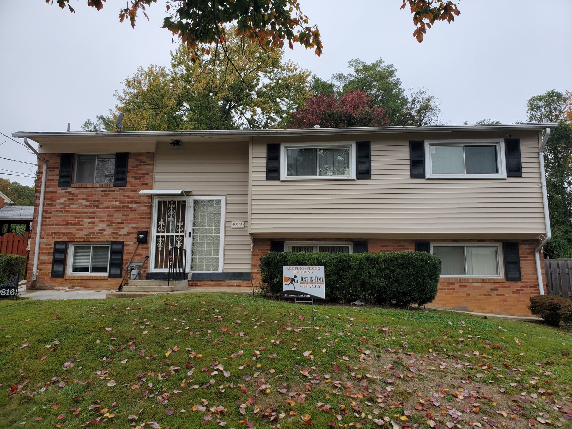 Two-story house with brick and siding, featuring windows, front door, and small yard with autumn leaves.