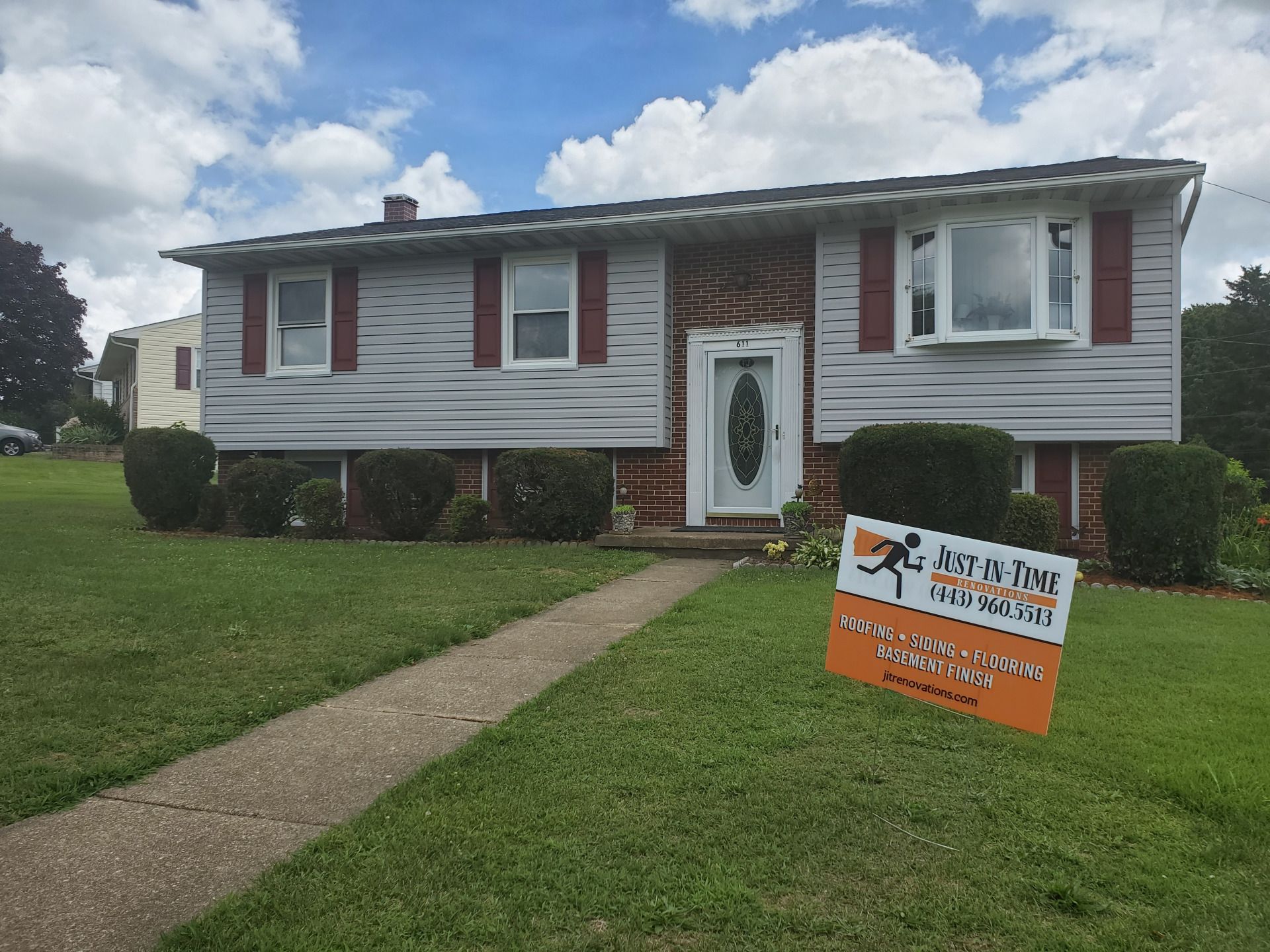 Ranch home with gray siding, red shutters, a walkway, and a sign on the lawn.