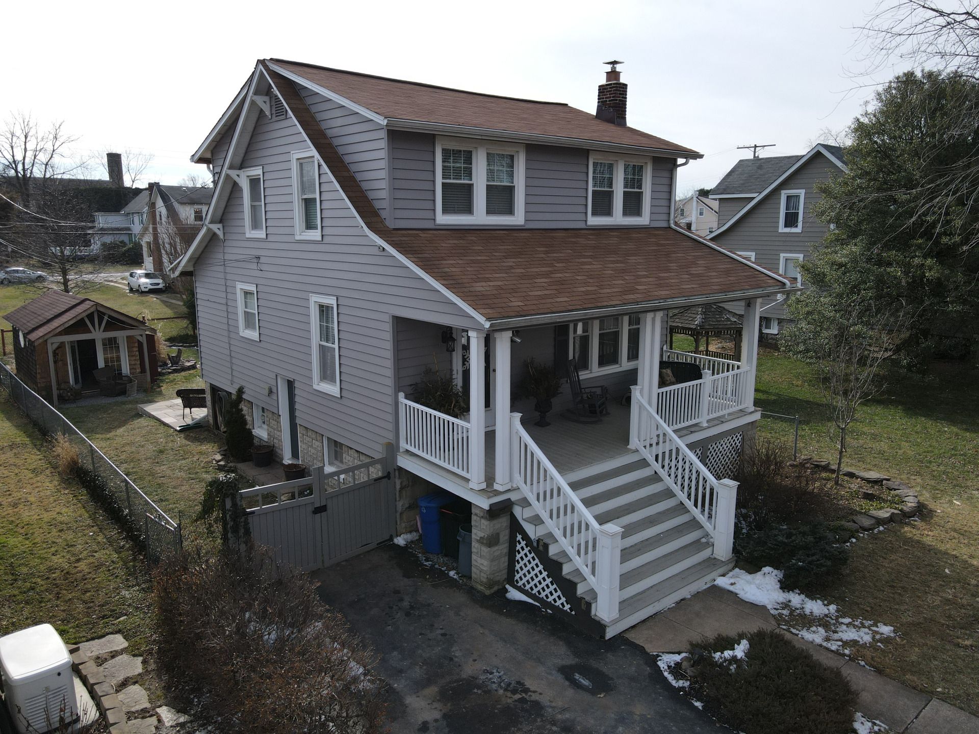 Two-story gray house with white porch, brown roof, and stairs. Driveway in front.