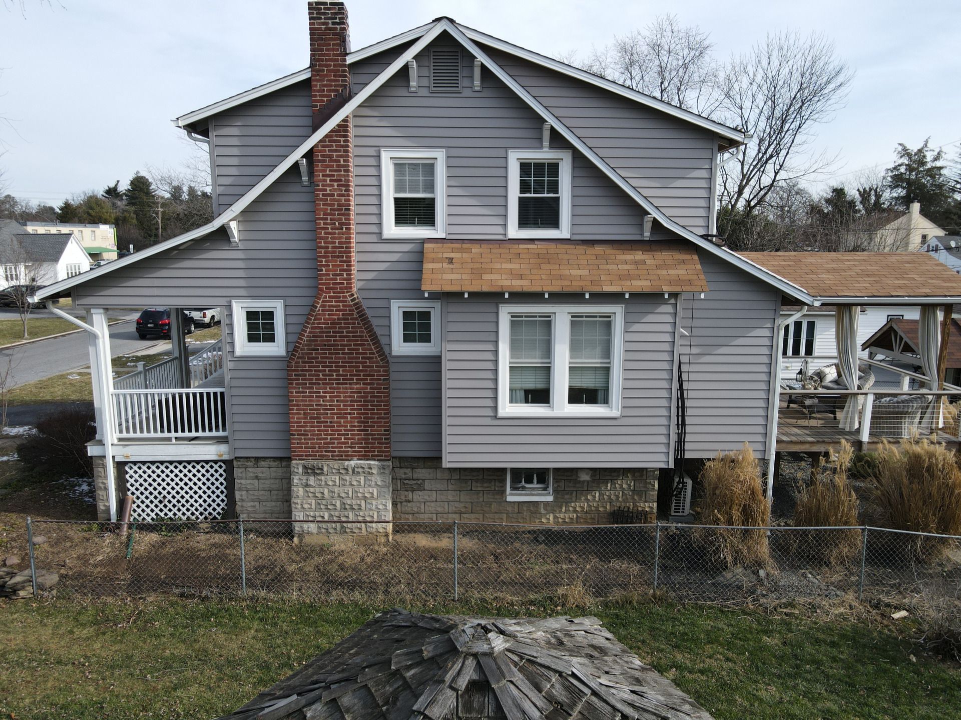 Gray two-story house with a brick chimney and white-framed windows. A small porch and yard.