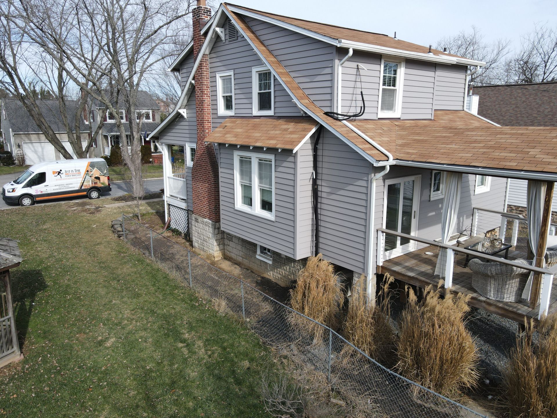 Gray house with brown roof, white trim, and deck. A van is parked in the yard.