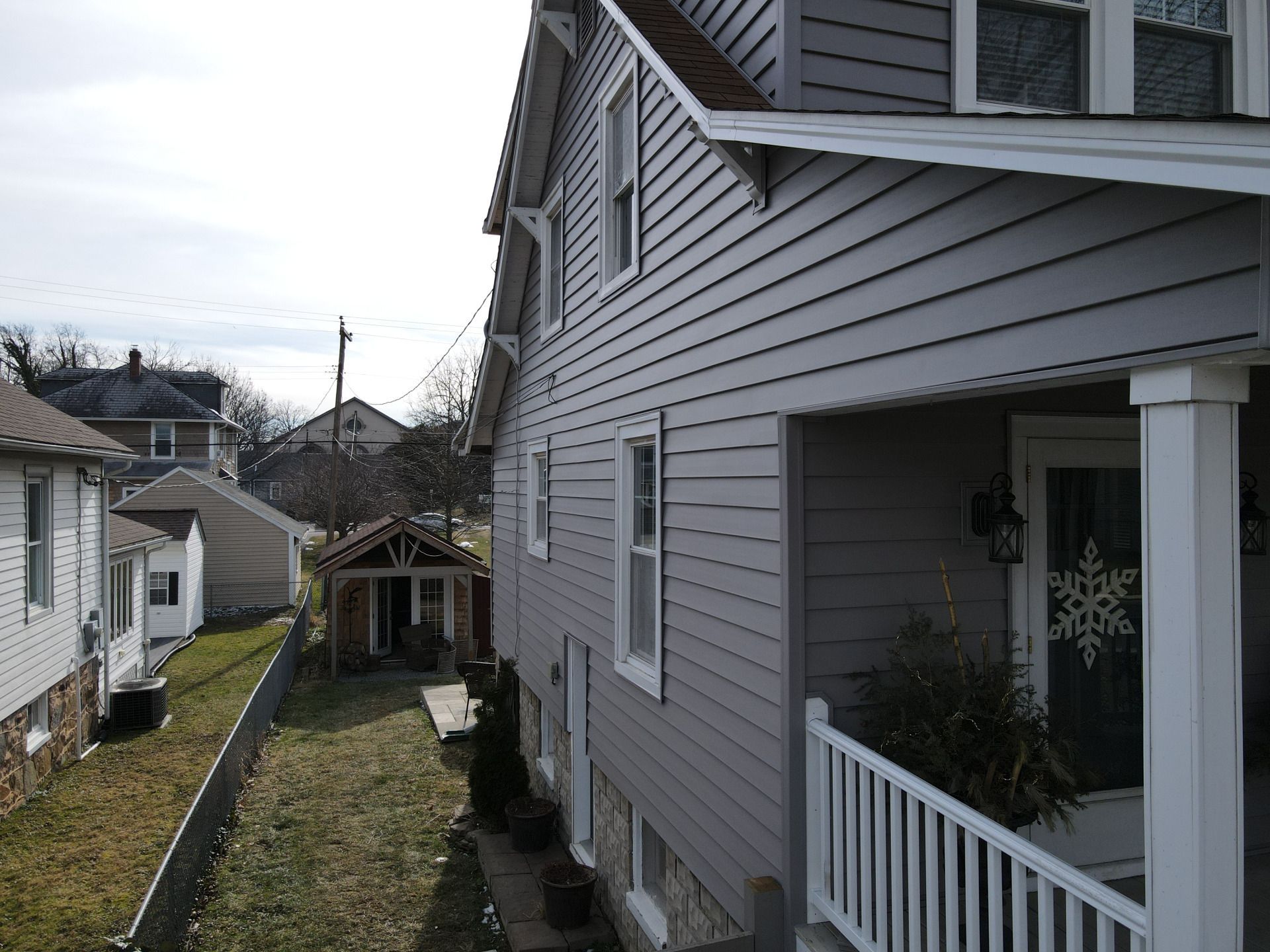 Side view of a gray house with a porch, and a yard with other houses in the background.