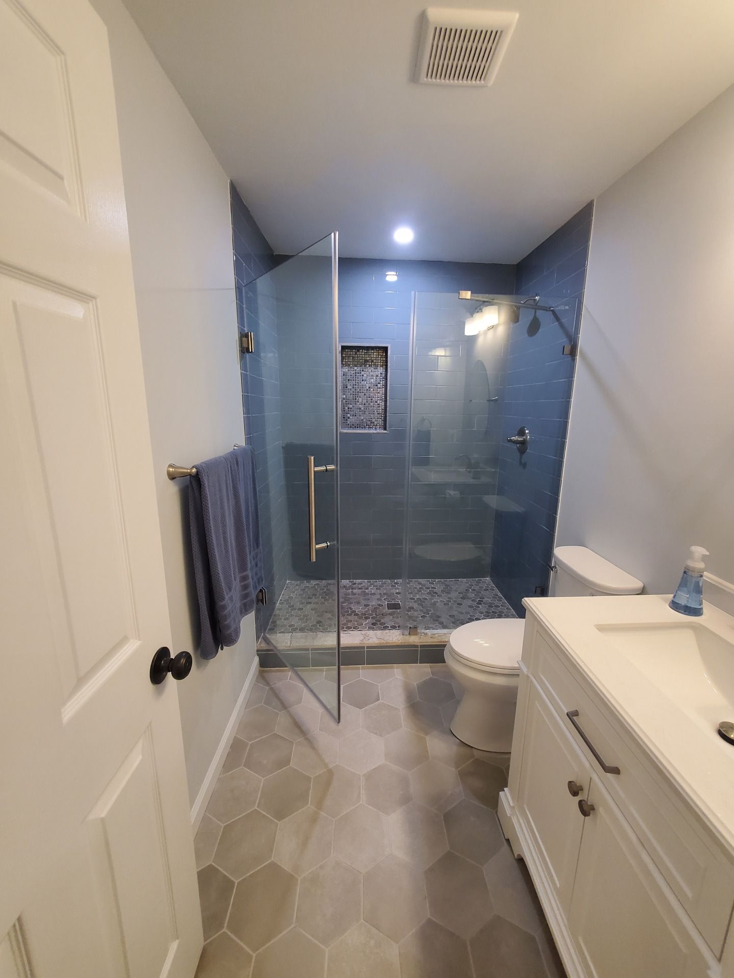 Modern bathroom with blue tiled shower, glass door, white vanity, and hexagon floor tiles.