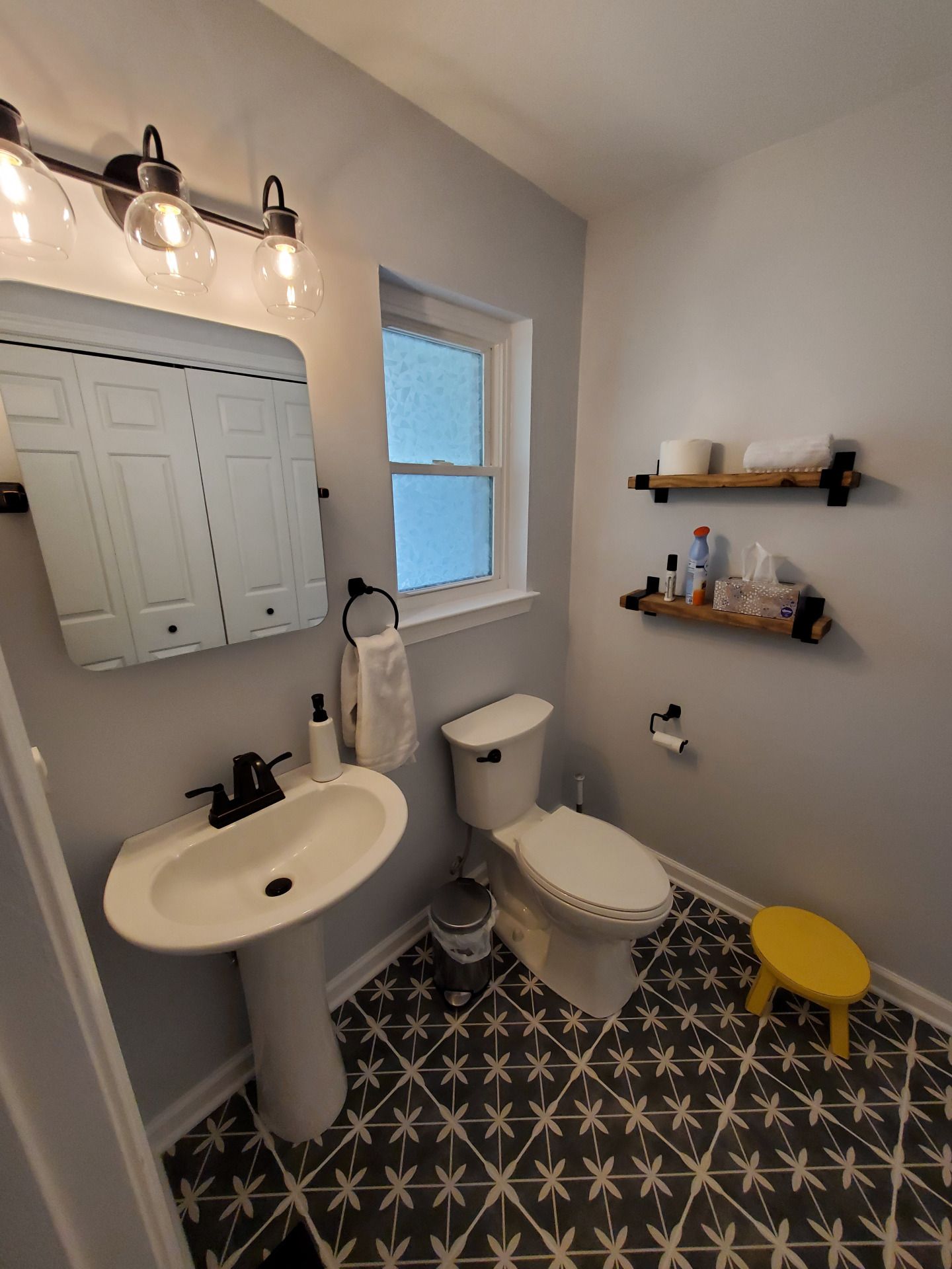 Small bathroom with pedestal sink, toilet, patterned tile floor, and medicine cabinet.