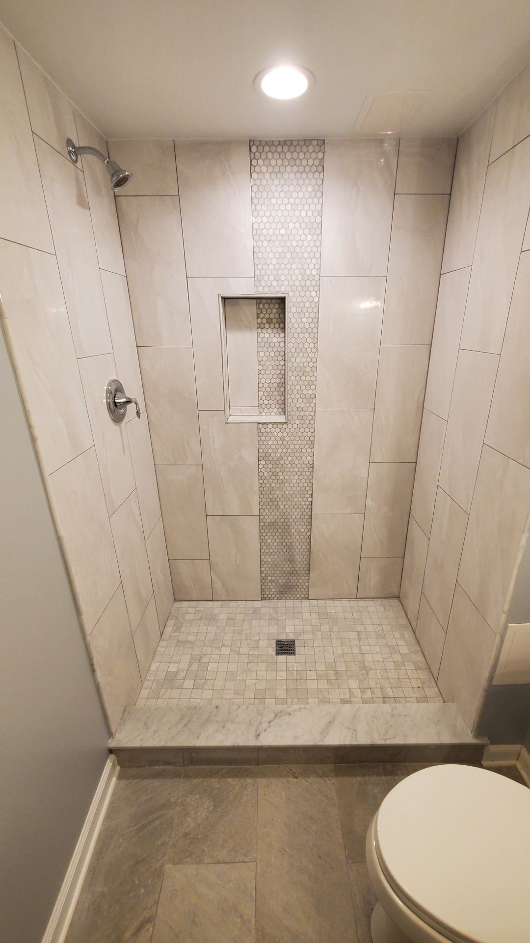 Modern walk-in shower with light-colored tiles, a mosaic accent, and a built-in shelf.