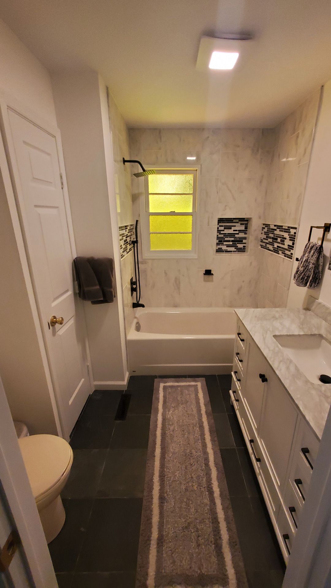 Narrow modern bathroom with white and gray tile, black floor, and a vanity.