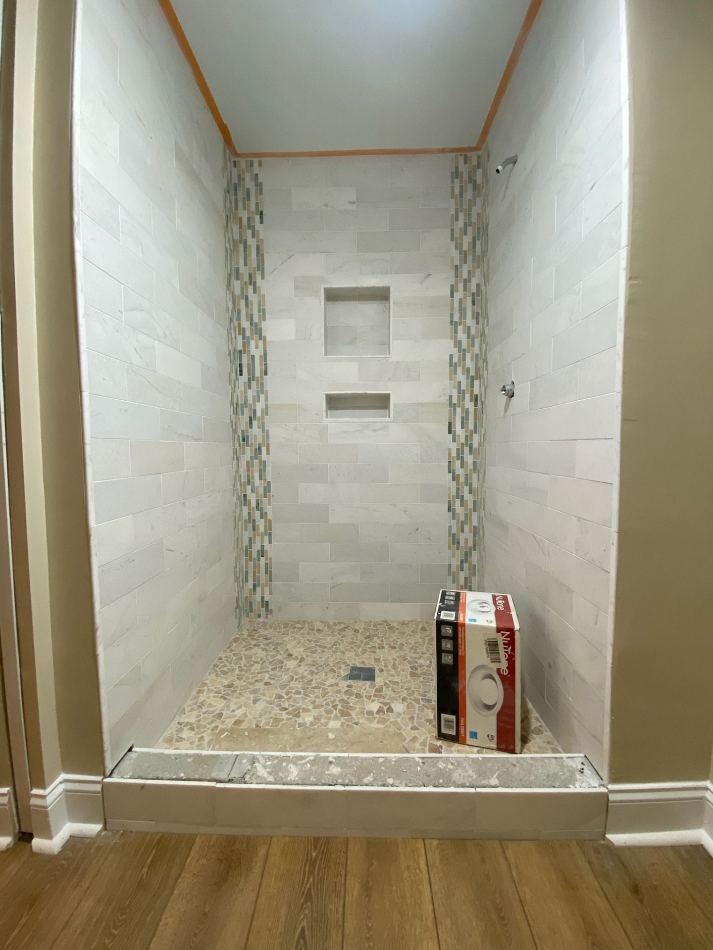 Newly tiled shower with stone floor, a box on the base, and contrasting decorative tile accents.