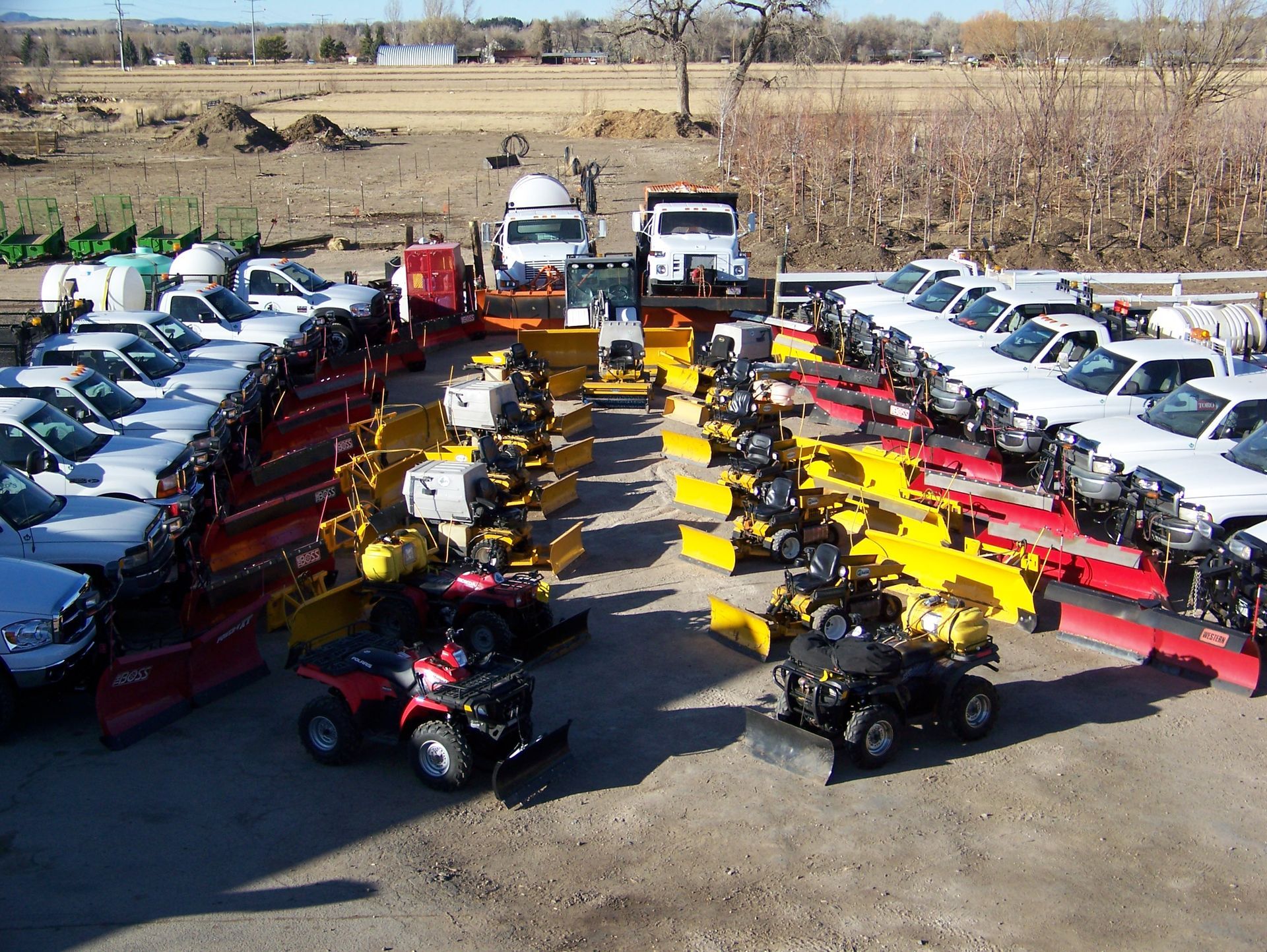 Fleet of snowplows, trucks, and ATVs in a lot, ready for winter.