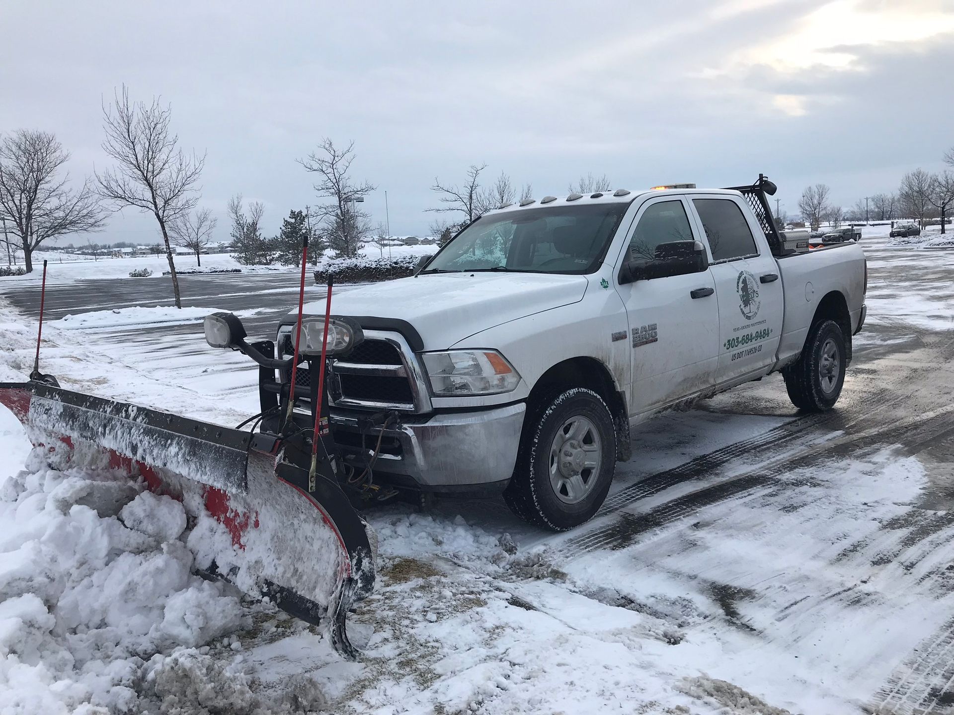 White truck plowing snow in a parking lot on a cloudy day.