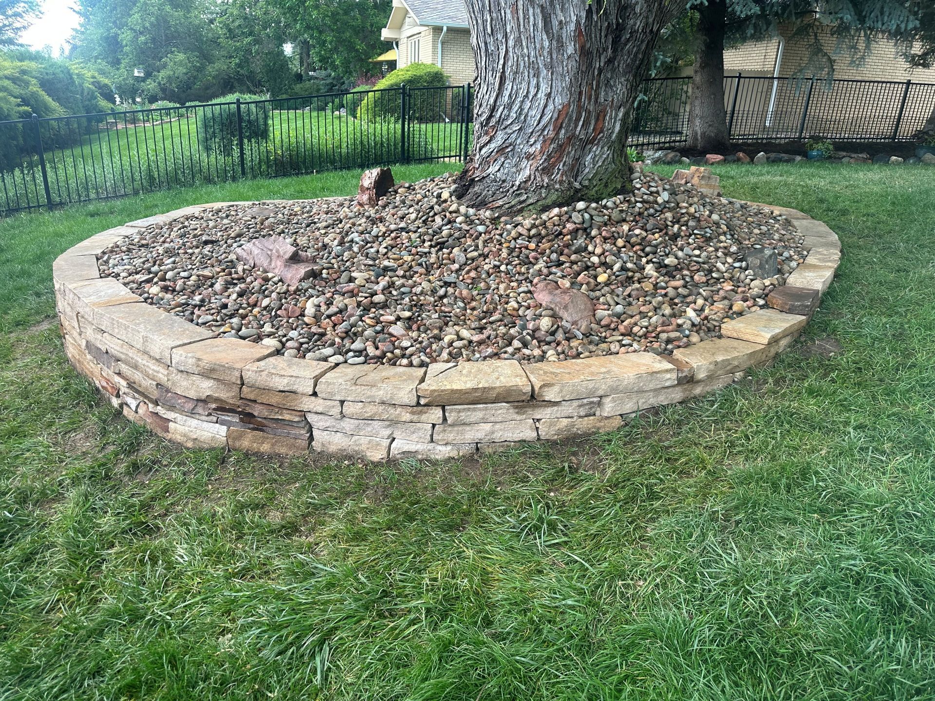 Circular stone-walled tree bed filled with gravel in a grassy yard.
