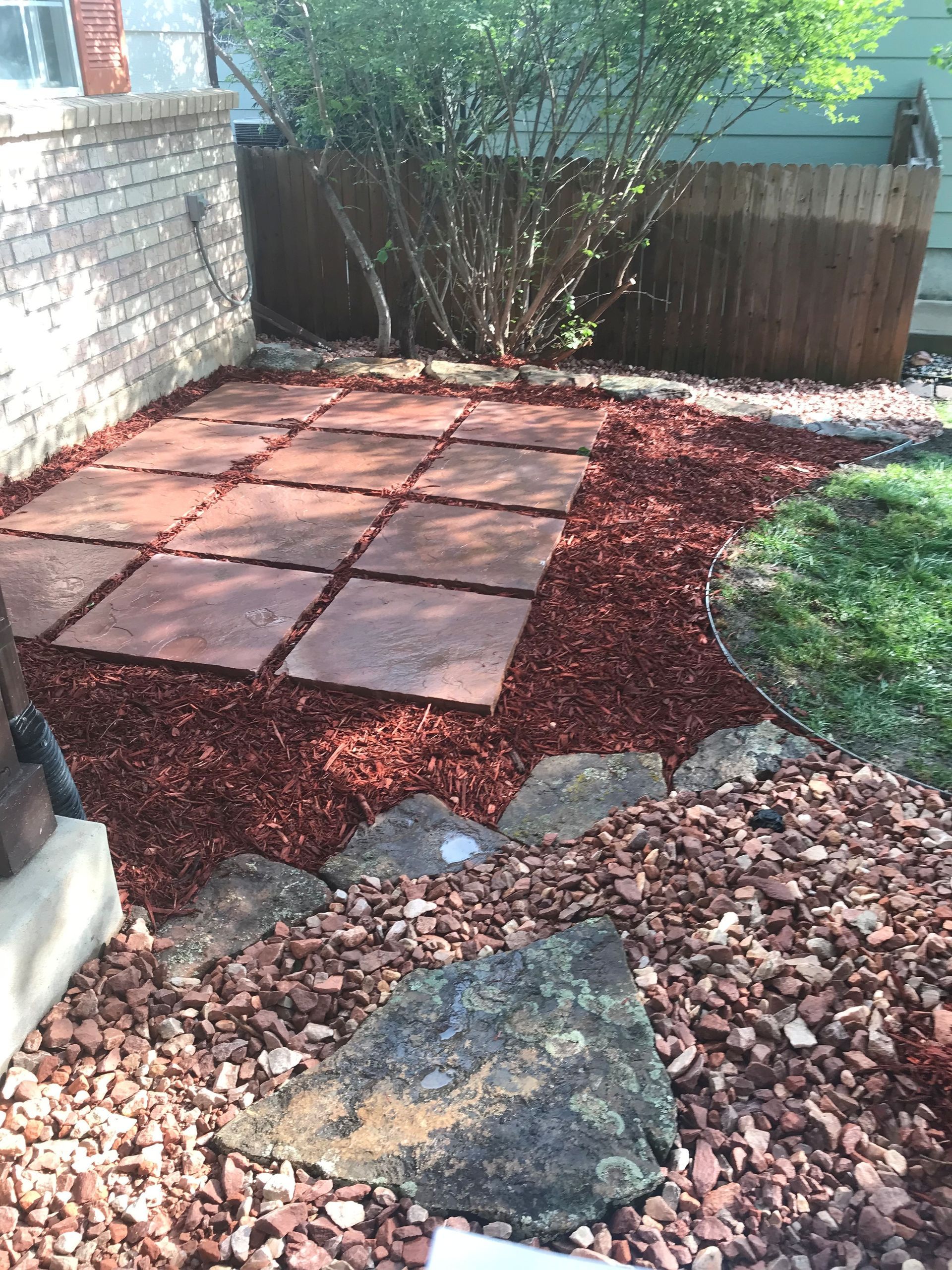 Brick patio with red mulch, stepping stones, and green shrubbery.