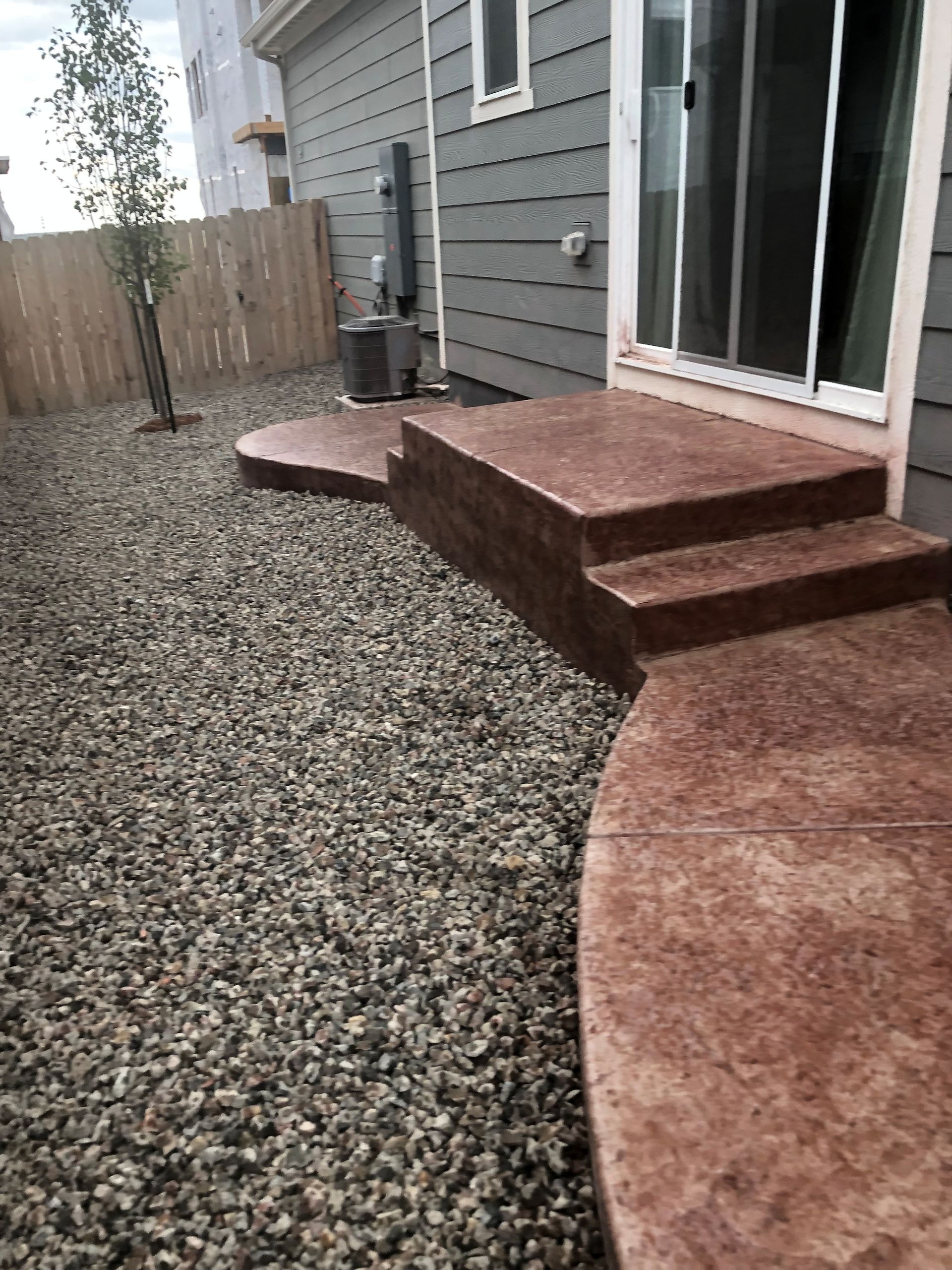 A concrete patio with steps, bordered by gravel, leads to a sliding glass door.