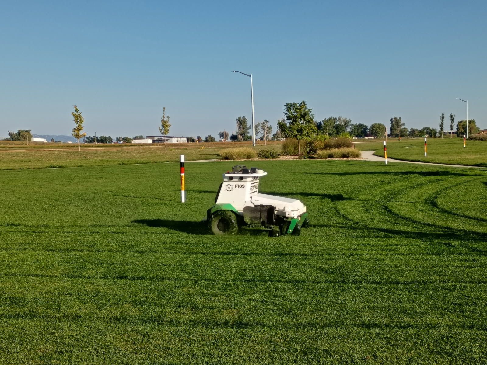 An autonomous lawnmower mows green grass in a park on a sunny day.